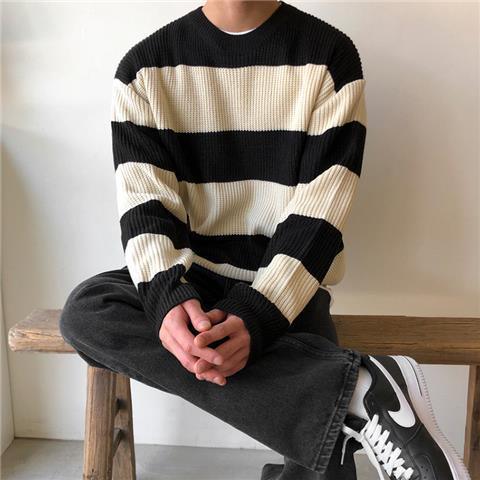 Person sitting on wooden bench wearing black and white striped sweater, dark jeans, and black white Nike sneakers