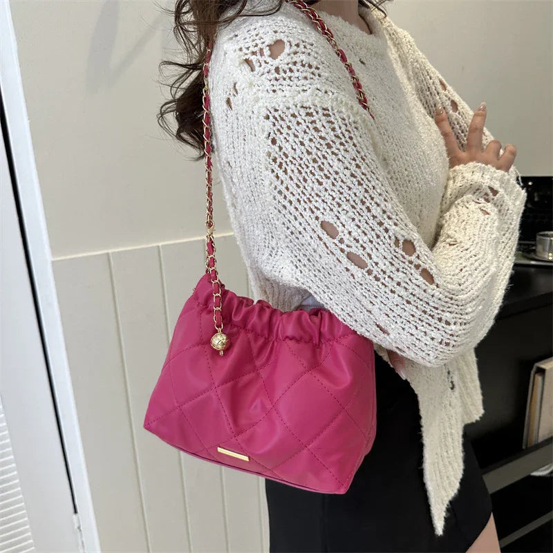 Woman wearing a white knit sweater and black skirt holding a pink quilted shoulder bag with gold chain strap