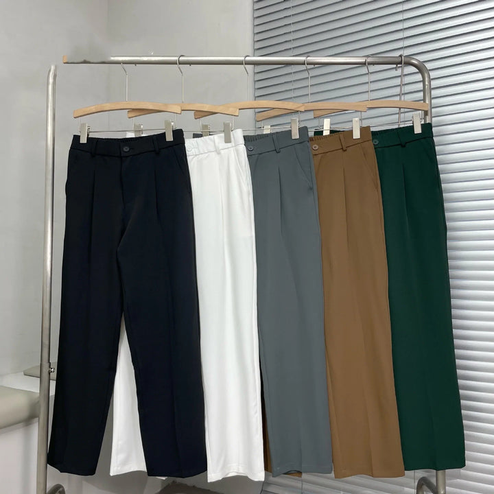 Five pairs of classic straight-leg dress pants in black, white, gray, brown, and green on wooden hangers