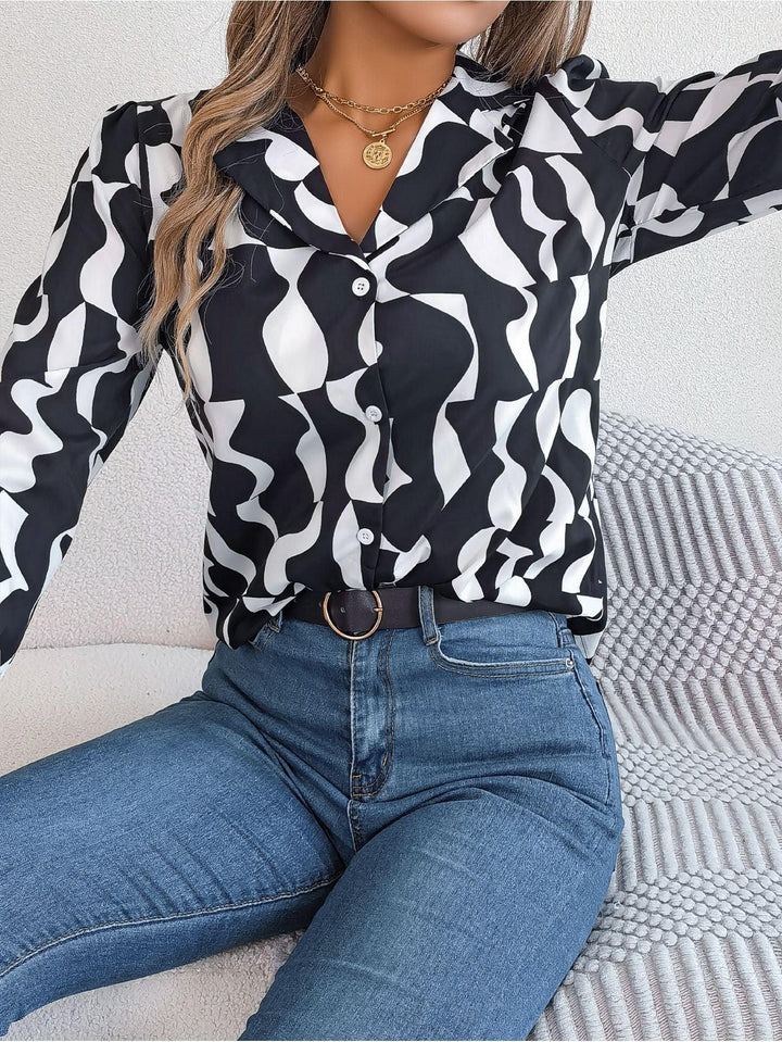 Woman wearing black and white abstract print button-up blouse with blue jeans and gold necklace sitting on textured cushion