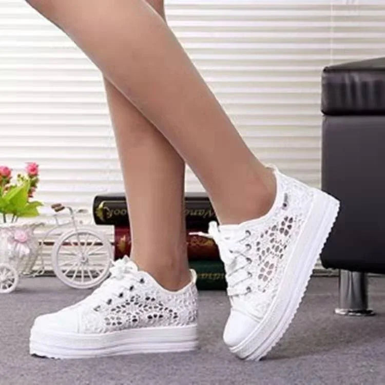 Womens white lace platform sneakers shown on legs indoors with decorative flower pot and books