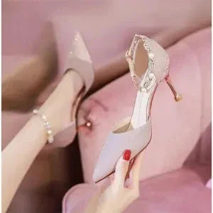 Elegant blush pink high-heeled shoes with pointed toes and ankle straps, styled on a soft pink chair