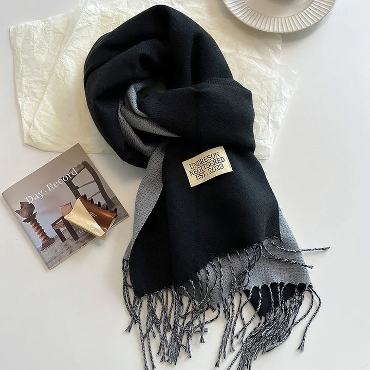 Black and gray fringed scarf with label on white surface next to magazine and plate