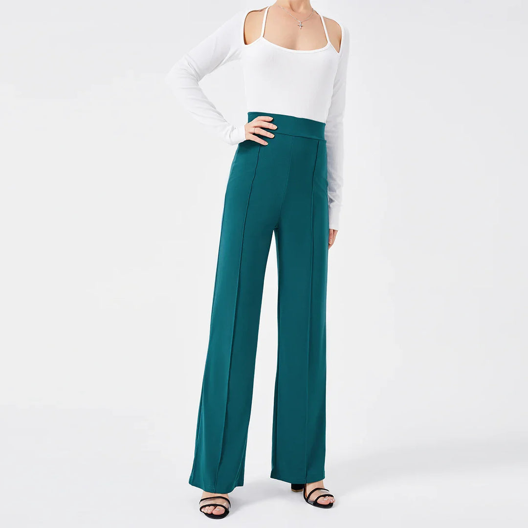 Woman wearing teal high-waisted trousers and white cold-shoulder long sleeve top with black heeled sandals