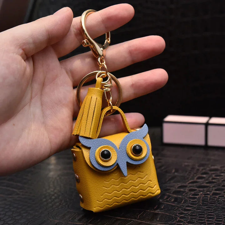 Hand holding yellow leather owl-shaped keychain with tassel and gold hardware