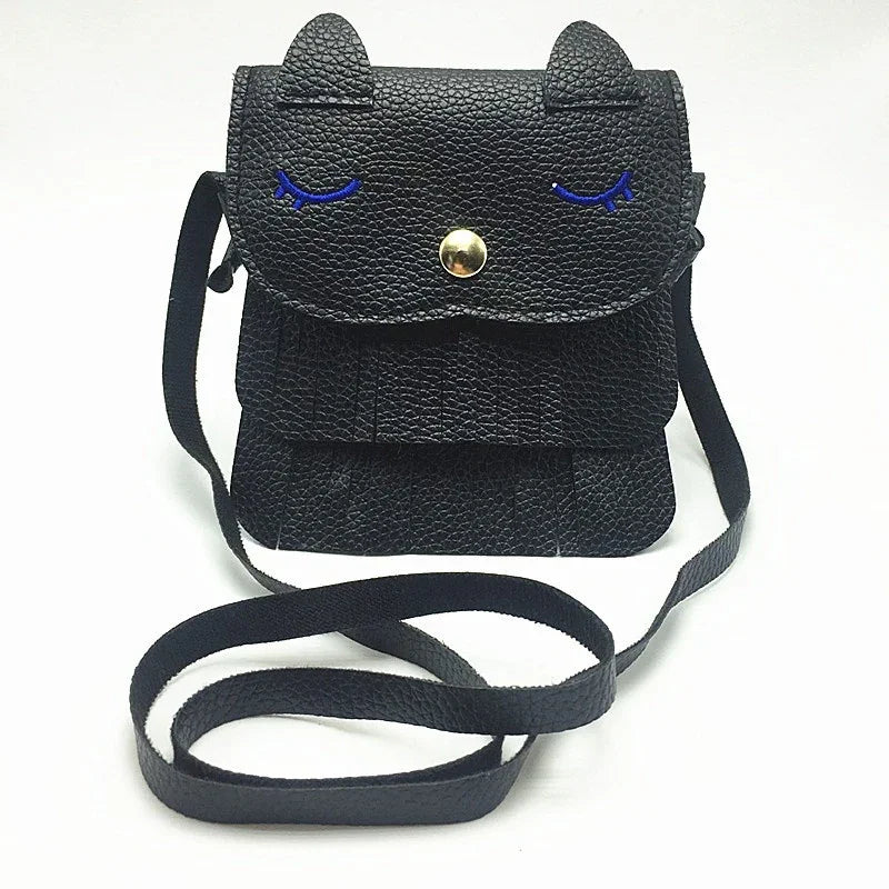 Black textured leather crossbody bag with cat ears, blue embroidered closed eyes, and gold snap button