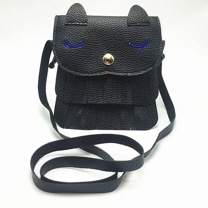 Black textured leather crossbody bag with cat ears, blue embroidered closed eyes, and gold snap button