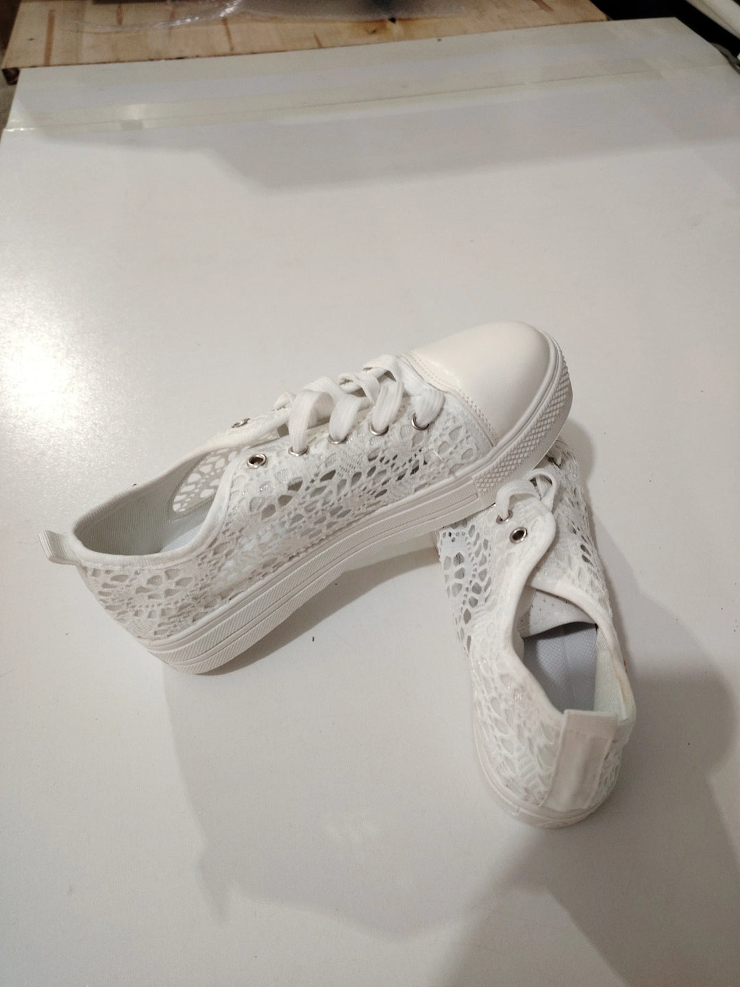 Pair of white lace casual sneakers with rubber toe caps and white laces on a light surface