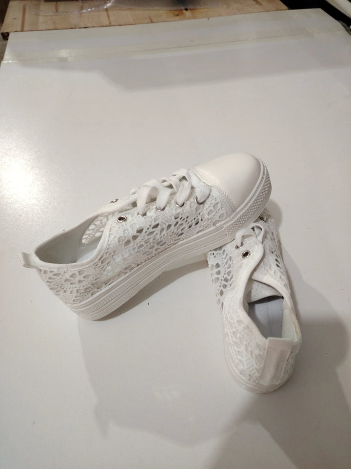 Pair of white lace casual sneakers with rubber toe caps and white laces on a light surface