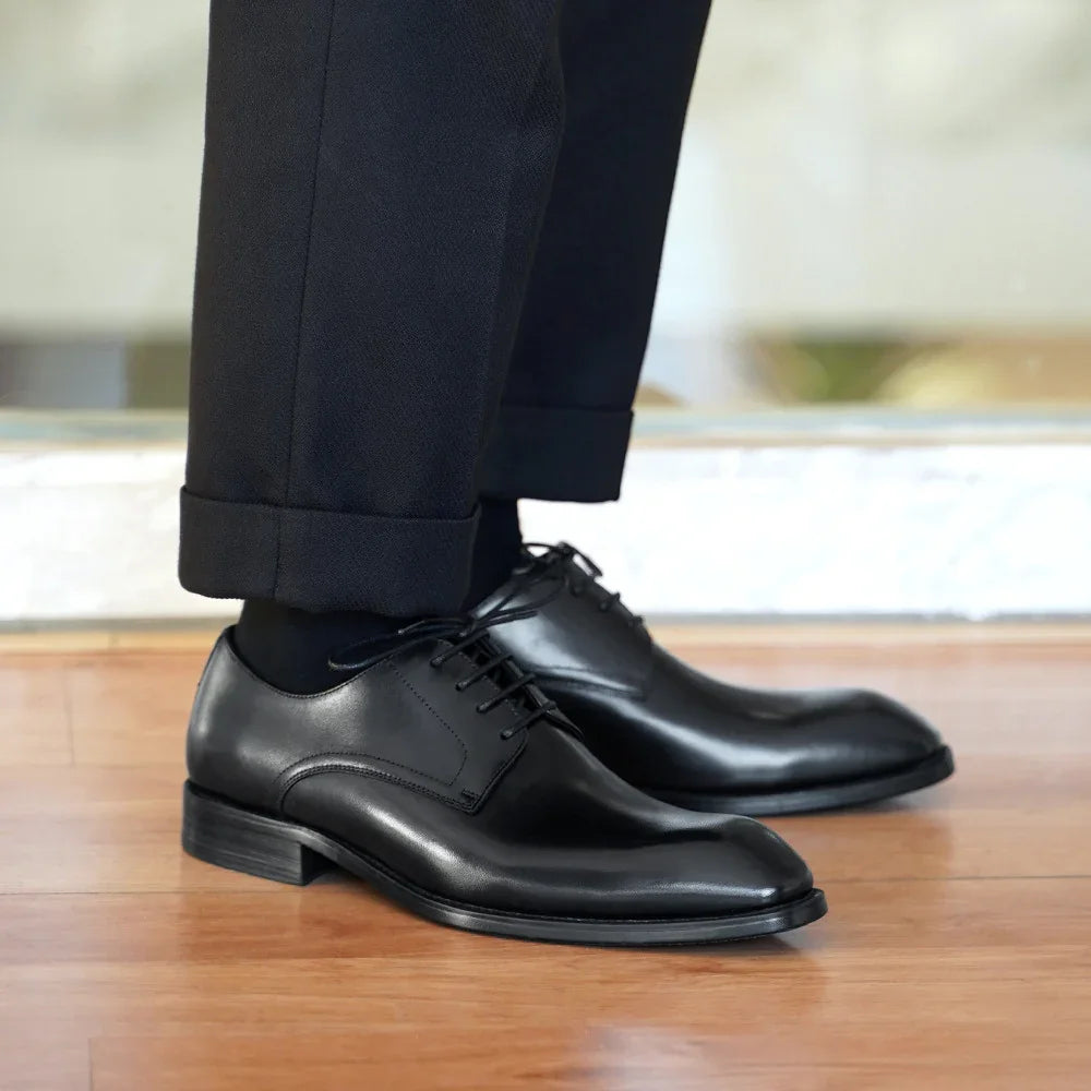 Close-up of polished black leather dress shoes worn with black trousers on wooden floor
