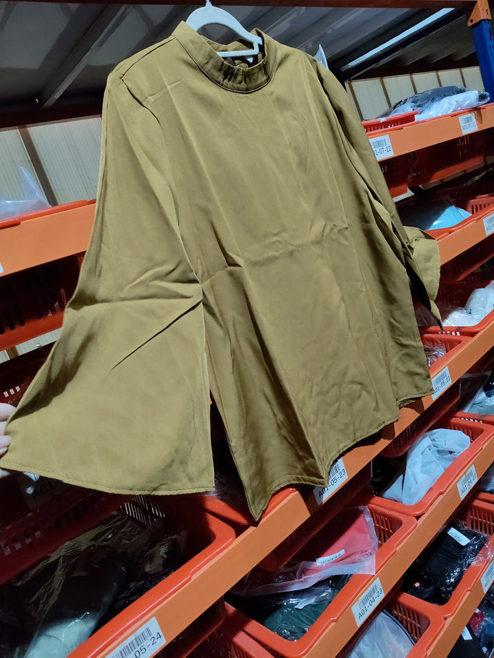 Light brown long-sleeve blouse with flared sleeves hanging on a white hanger in a warehouse with orange storage bins