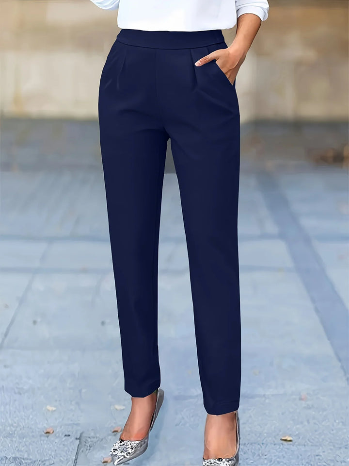 Woman wearing navy blue tapered dress pants with pleats and silver pointed heels