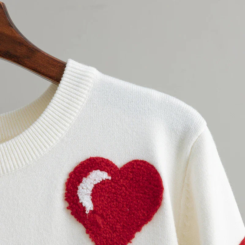 White knitted sweater with a textured red heart patch on chest hanging on wooden hanger