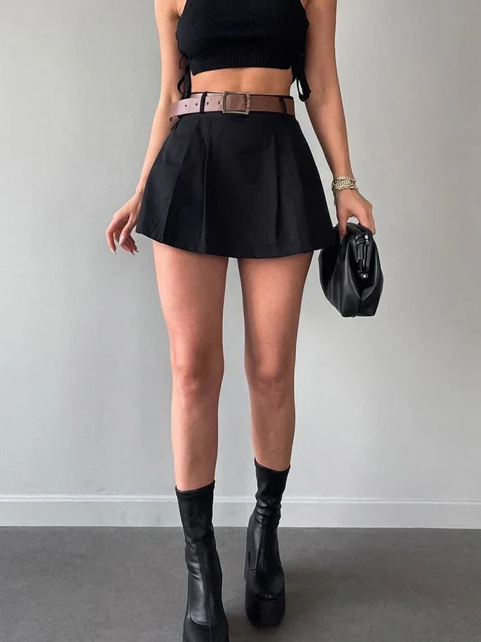 Woman wearing black crop top, high-waisted black mini skirt with brown belt, and black platform boots holding black purse