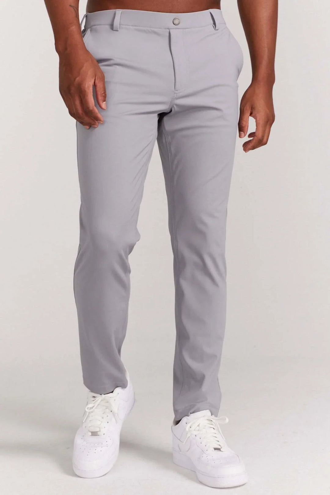 Male model wearing fitted light gray pants and white sneakers against plain white background