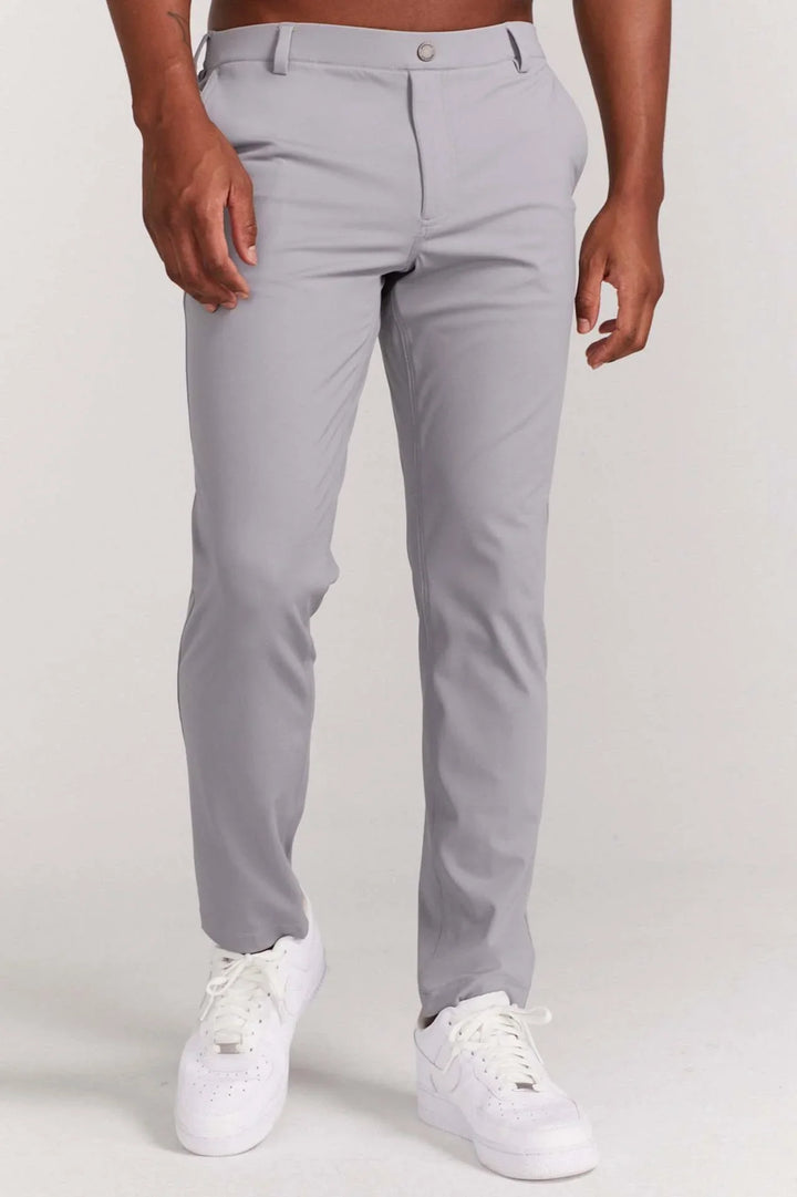 Male model wearing fitted light gray pants and white sneakers against plain white background
