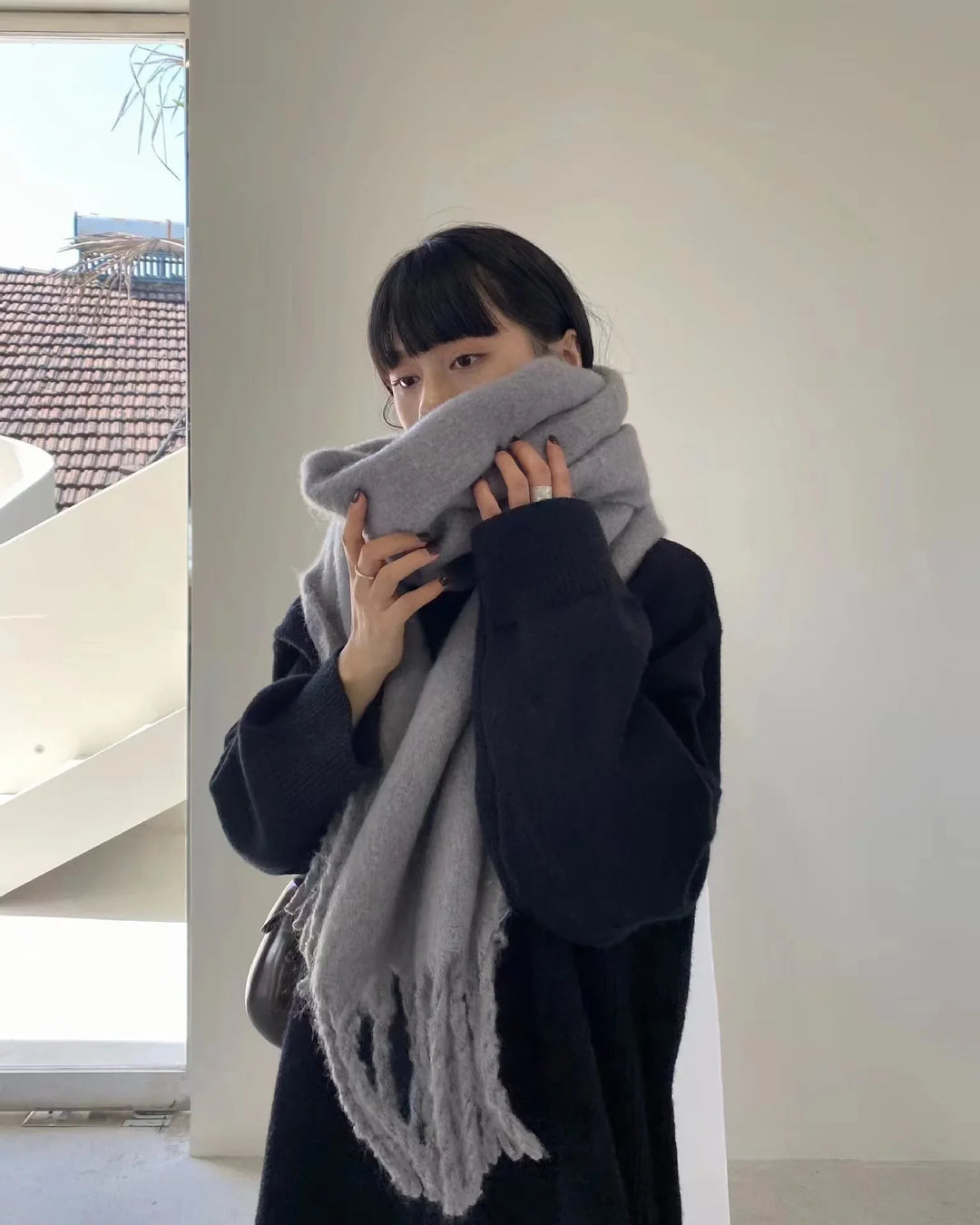Woman indoors wearing oversized black sweater and large grey scarf with fringes
