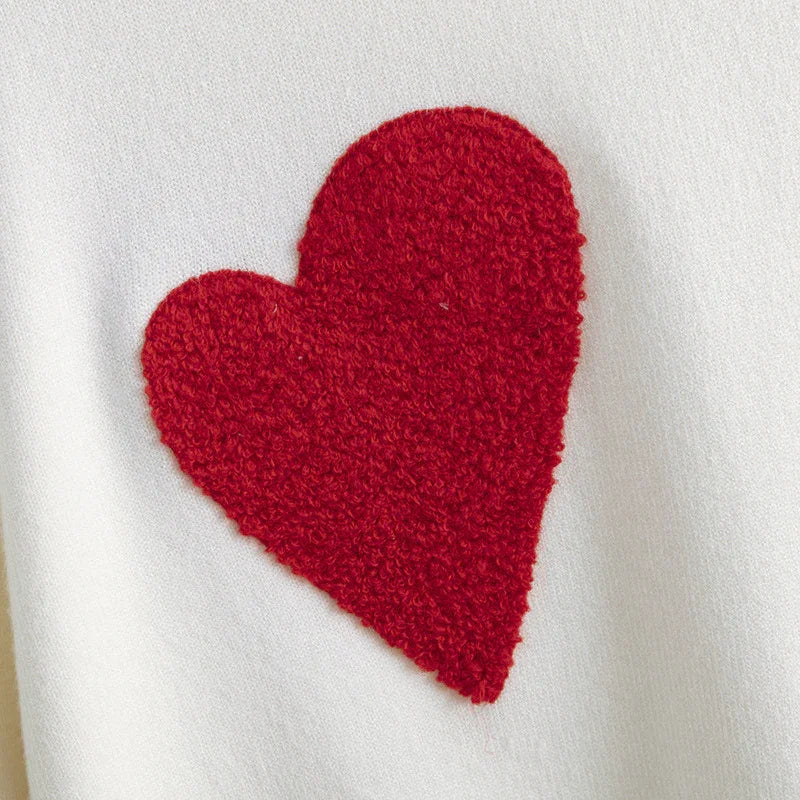 Close-up of white fabric with a textured red heart appliqué, cozy knit textile detail