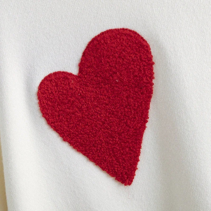 Close-up of white fabric with a textured red heart appliqué, cozy knit textile detail