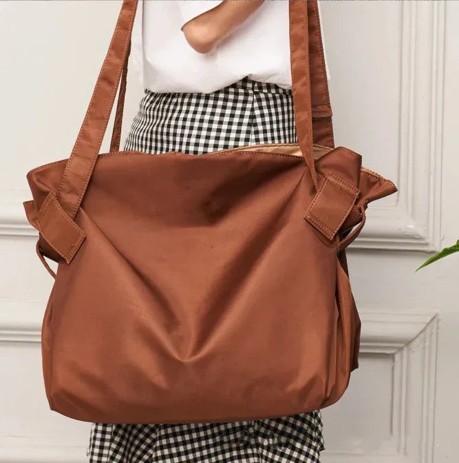 brown oversized tote bag worn by person in black and white checkered skirt against white paneled wall