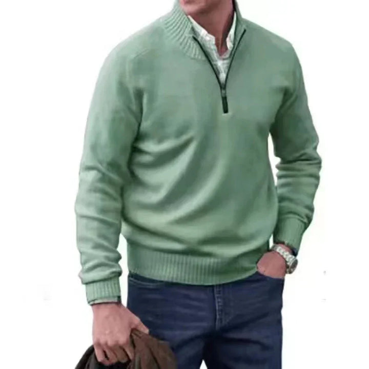 Man wearing a light green quarter-zip sweater with a white shirt underneath and dark blue jeans