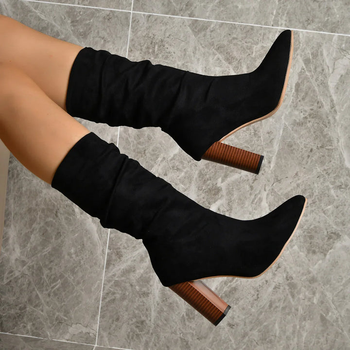 Black suede knee-high boots with block wooden heels on marble floor
