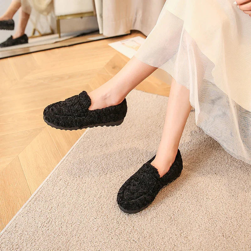 Woman wearing black fuzzy slip-on slippers sitting on carpet near wooden floor