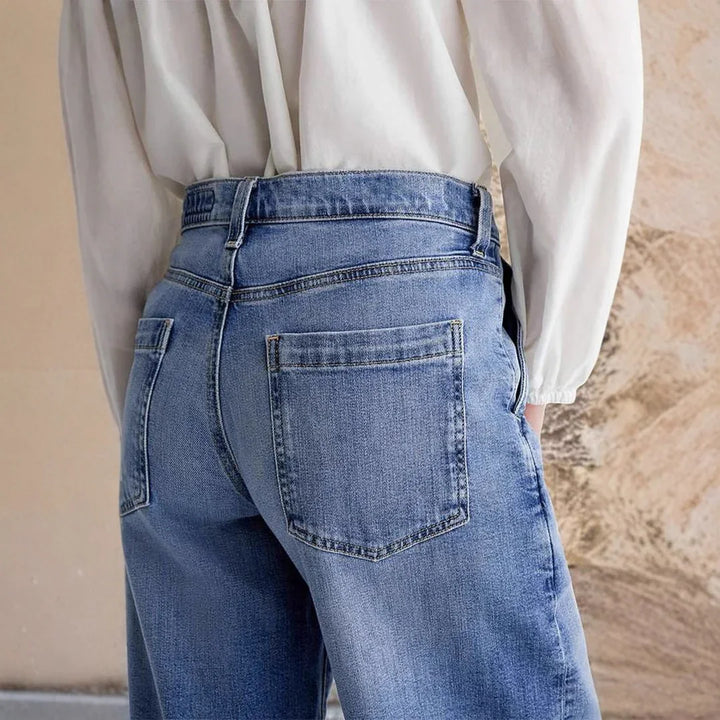 Close-up of person wearing blue denim jeans and white blouse against textured beige wall