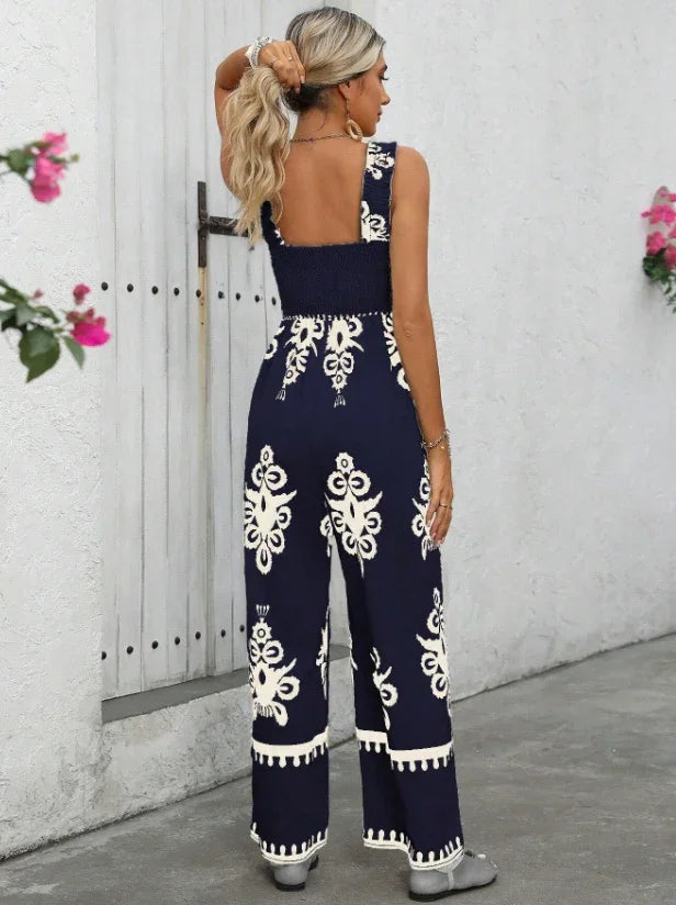 Woman wearing navy blue and white floral print wide-leg jumpsuit with square back and sleeveless design near white door