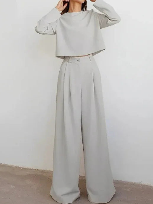 Woman wearing stylish light beige wide-leg pants and matching long-sleeve cropped top against white wall