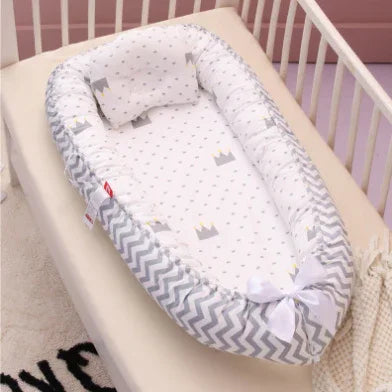 Baby nest crib with gray chevron pattern and crown print pillow inside white wooden crib