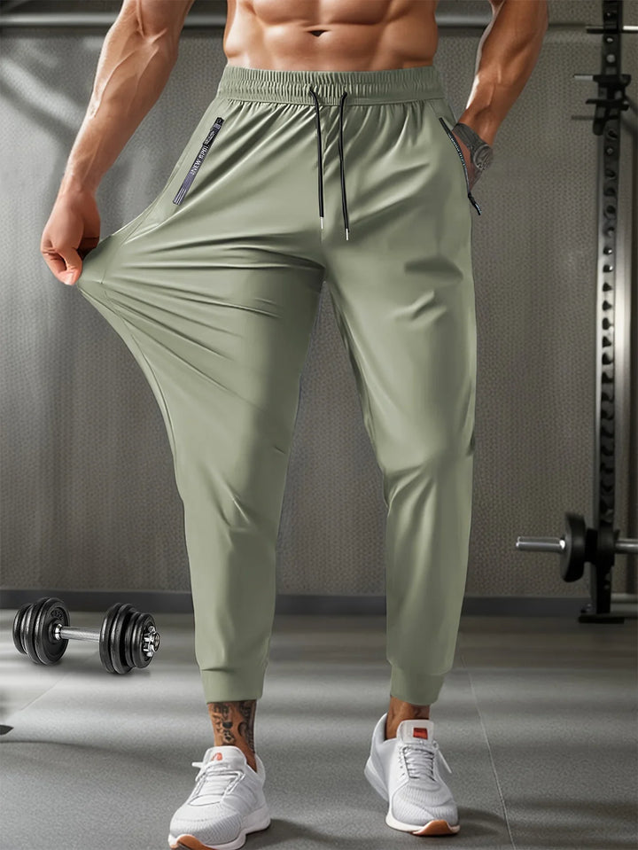 Muscular man in gym wearing olive green stretchy jogger pants and white sneakers stretching fabric