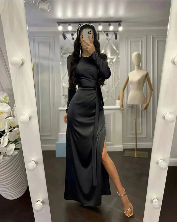 Woman wearing a sleek black long-sleeve evening gown with a thigh-high slit, taking a mirror selfie