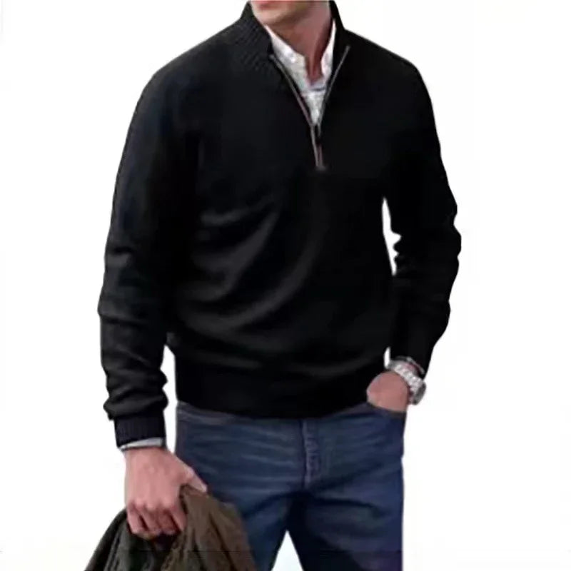 Man wearing black quarter-zip pullover sweater with blue jeans holding brown jacket