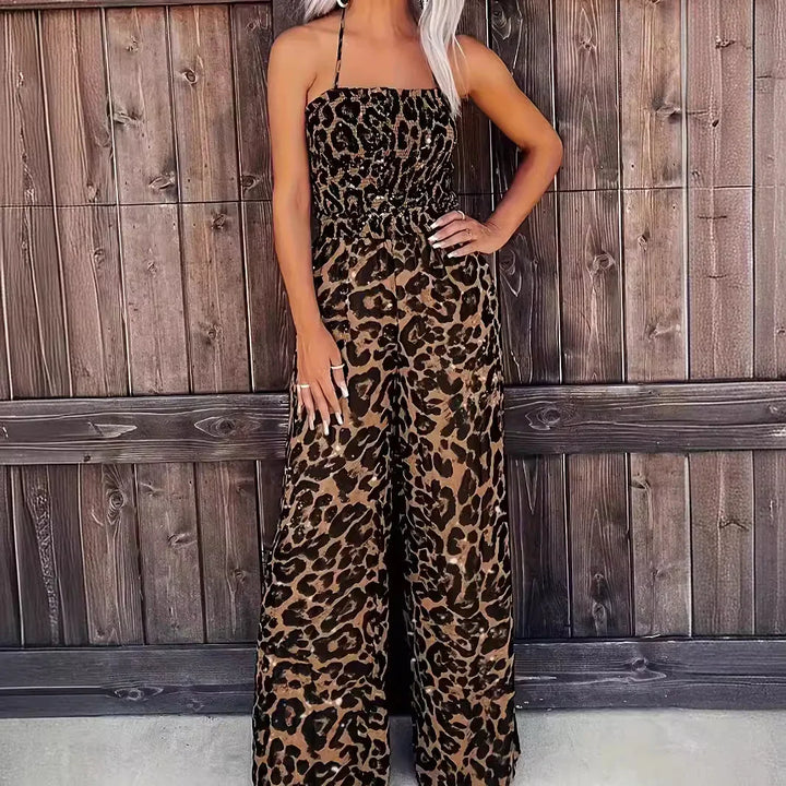 Woman wearing brown and black leopard print wide-leg jumpsuit with halter neck standing against wooden wall