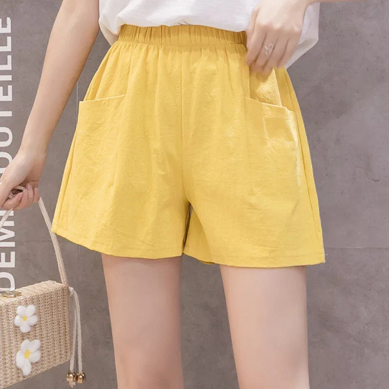 Woman wearing casual yellow elastic waist shorts with front pockets and white top holding flower-adorned woven bag