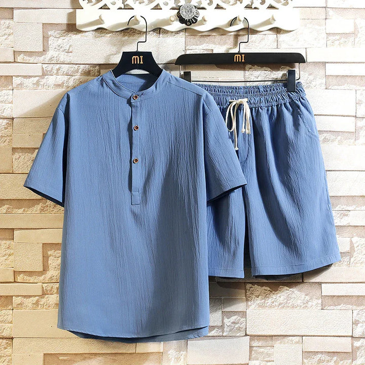 Light blue short sleeve mandarin collar shirt and matching elastic waist shorts set on hangers against stone wall