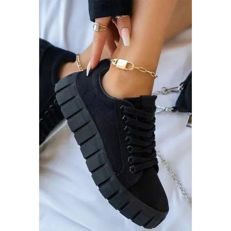 Black platform sneakers with chunky soles worn with gold chain anklets and manicured nails