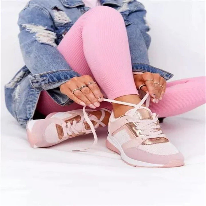 Person wearing pink leggings and a ripped denim jacket tying white and pink sneakers with metallic rose gold accents