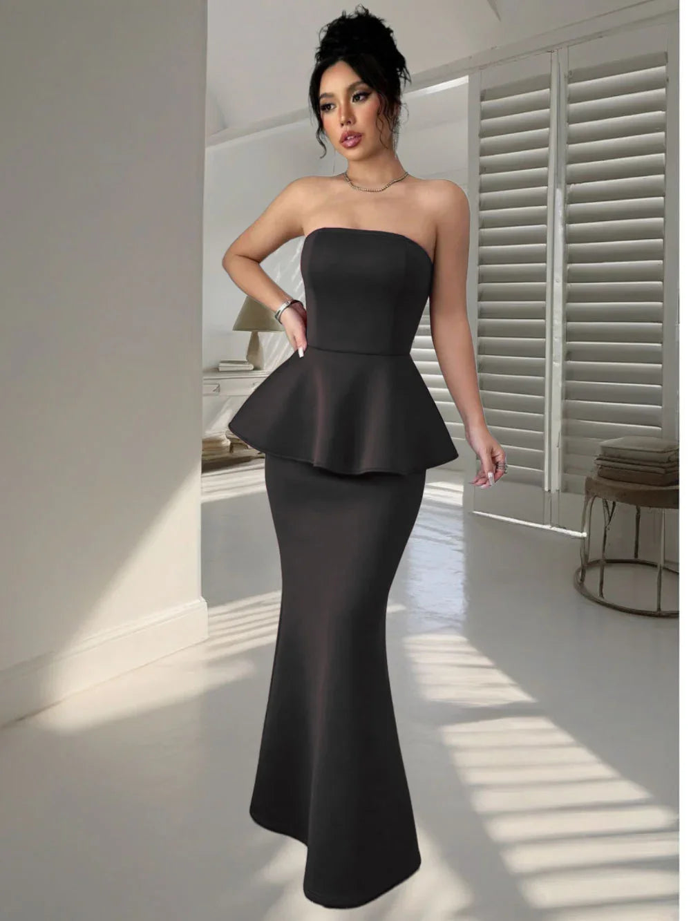 woman in strapless black mermaid peplum evening gown in bright room with white shutters
