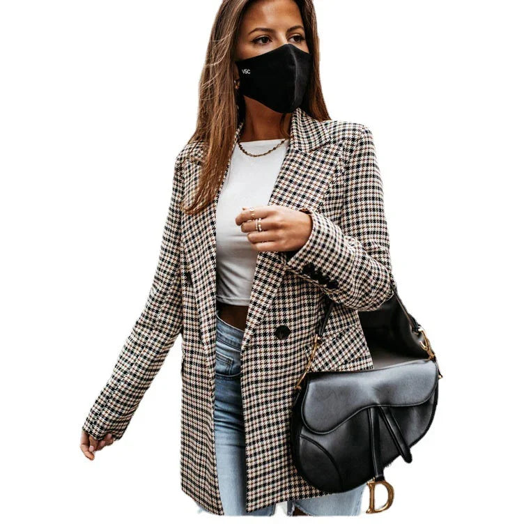 Woman wearing houndstooth blazer, white top, blue jeans, black face mask, and black designer saddle bag