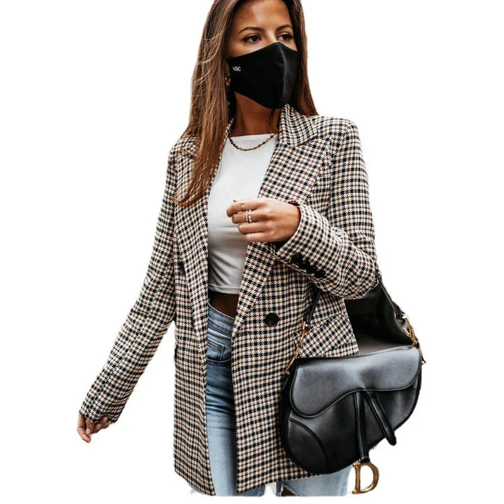 Woman wearing houndstooth blazer, white top, blue jeans, black face mask, and black designer saddle bag