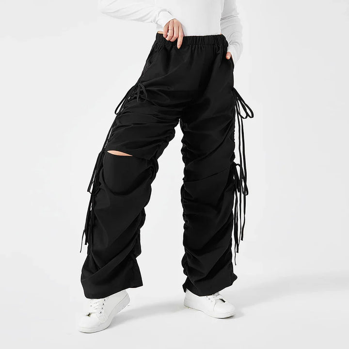 Woman wearing black ruched cargo pants with side ties and white sneakers on white background