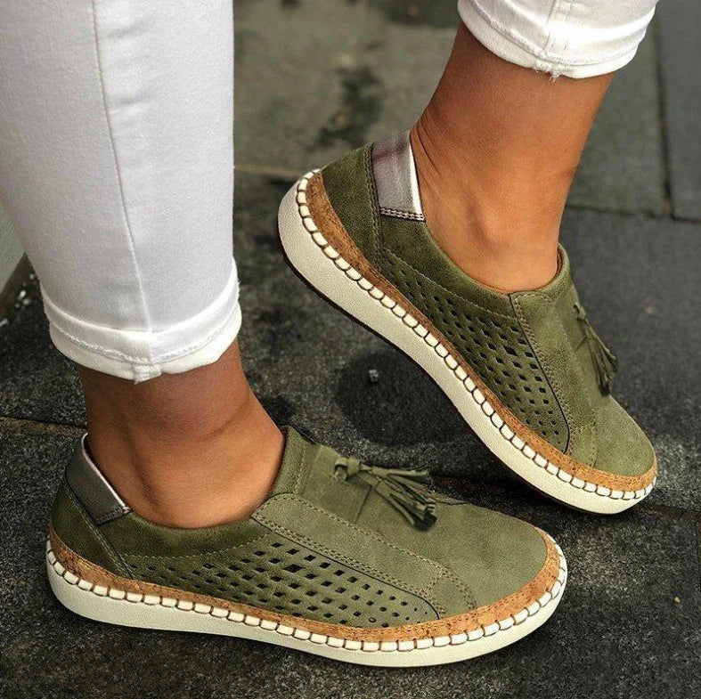 Casual olive green perforated suede slip-on sneakers with tassels and white soles worn with white pants