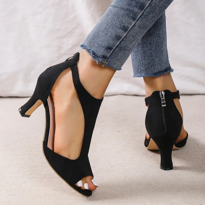 Black suede open-toe heels with back zipper worn with frayed hem blue jeans on beige floor