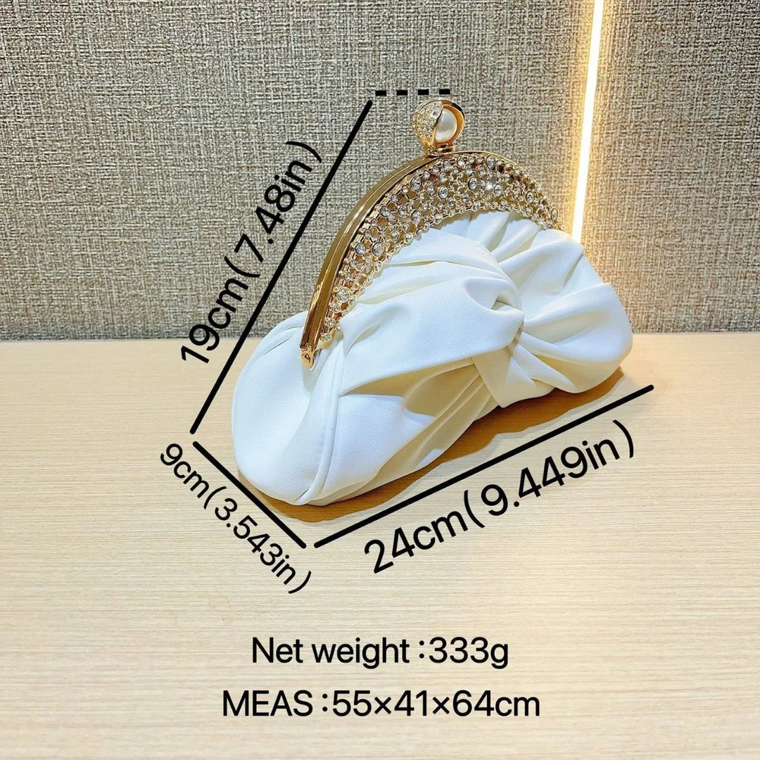 White ruched satin clutch bag with gold crystal-studded frame and pearl clasp on wooden surface