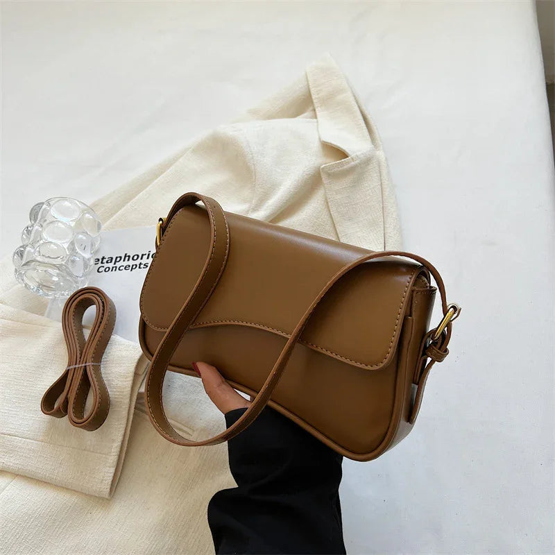 Brown leather crossbody bag held over beige fabric jacket with extra strap and clear glass candle holder