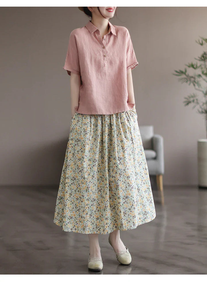 woman wearing pink short-sleeve blouse and floral midi skirt standing indoors with modern decor