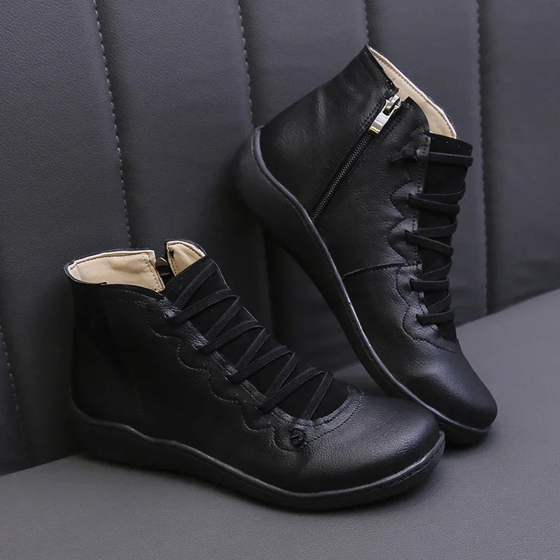 Black leather ankle boots with side zipper and scalloped lace-up design on gray textured background