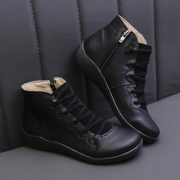 Black leather ankle boots with side zipper and scalloped lace-up design on gray textured background